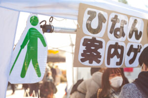 イベント用テントに、ひなん案内ゲームの看板と白杖を持って歩くピクトグラムが吊り下がっている。