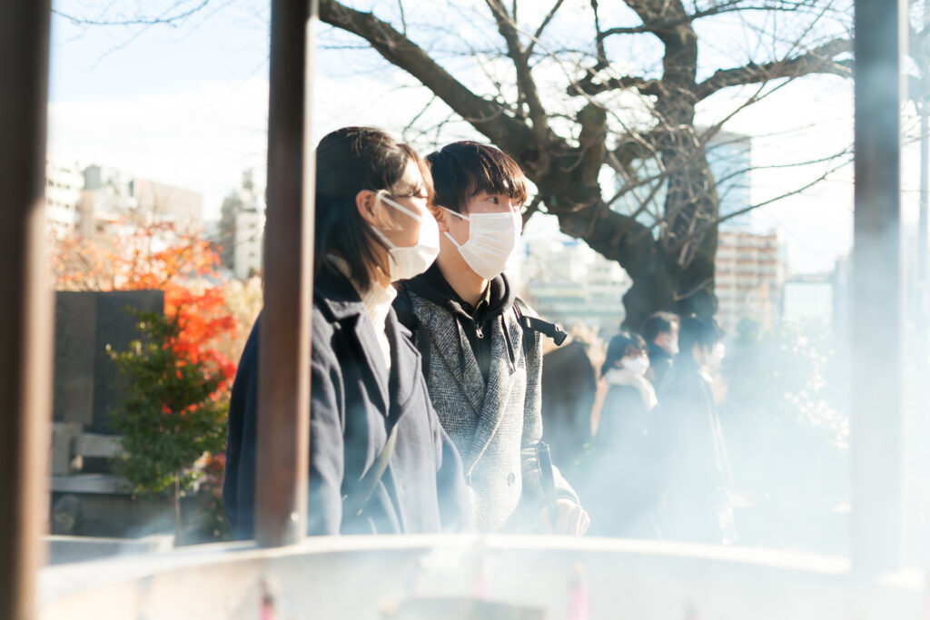 上野、不忍池弁天堂の香炉の横に立つ北原さんと谷越さん。香炉からは線香の煙が立ちのぼっている。