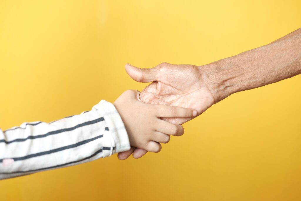 子どもの手と大人の手が、明るい室内で握手している。