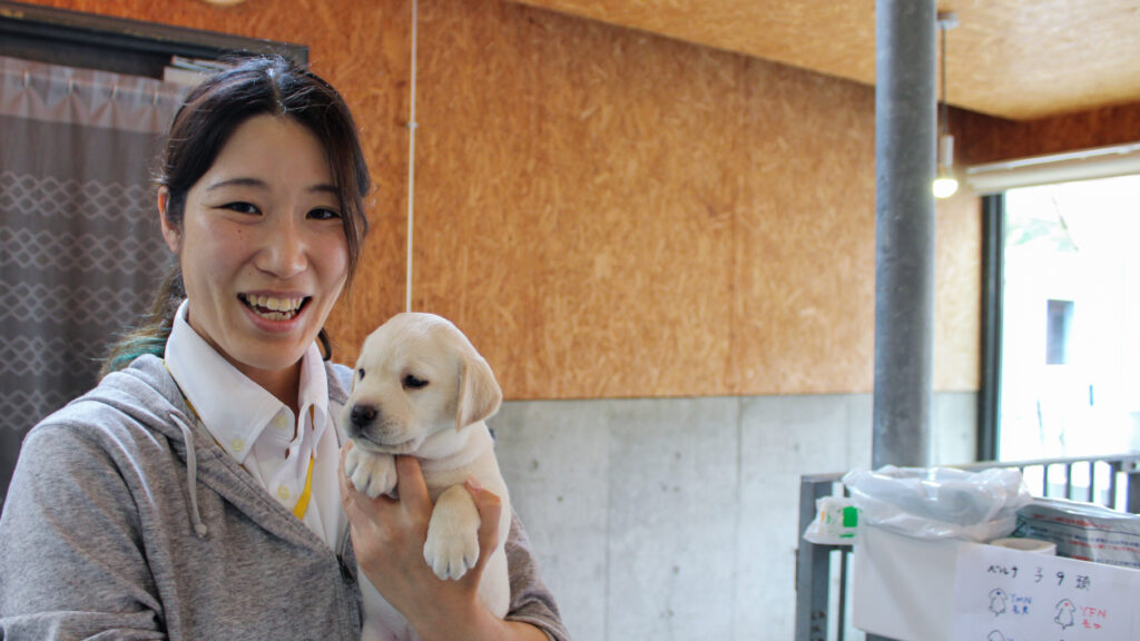 レトリバーの子犬を抱っこしながら笑顔の本岡さん。
