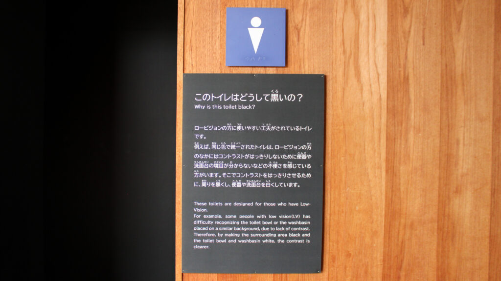 「このトイレはどうして黒いの？ロービジョンの方に見えやすいため」と書かれたボード。日本語と英語表記があります。