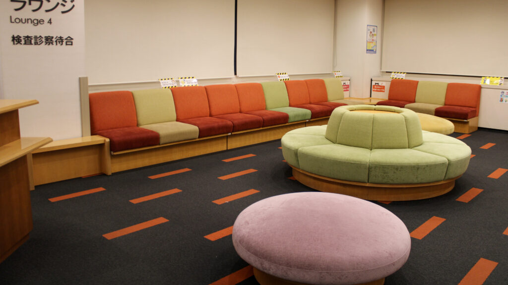 色鮮やかなオレンジとミントグリーンのソファや、丸い形のピンク色の大きなソファーがある井上眼科の待合室。