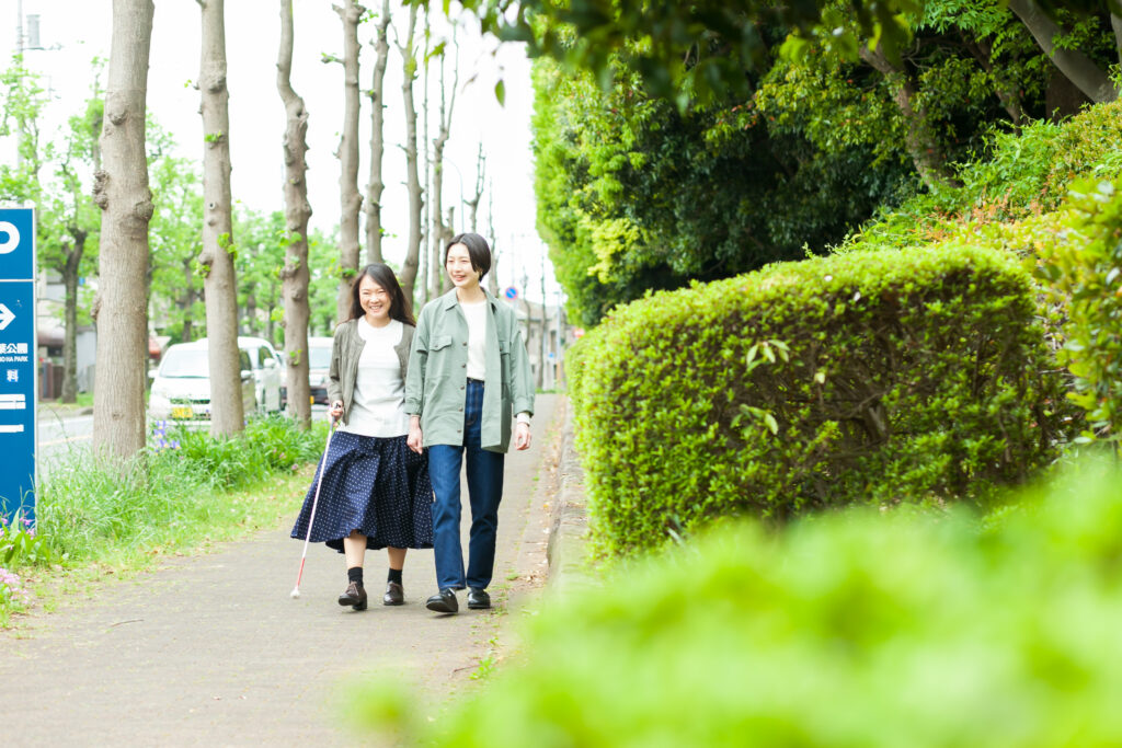 笑顔で話しながら、並木道を歩く視覚障害者とガイドヘルパー。