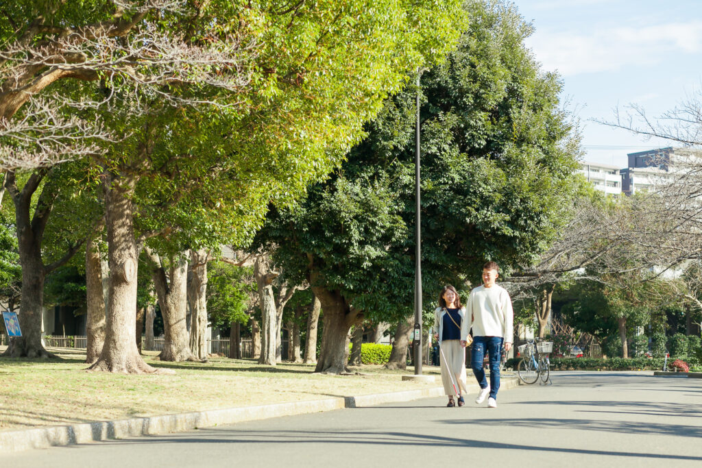 緑の多い公園内で、視覚障害者を誘導している高橋さん。