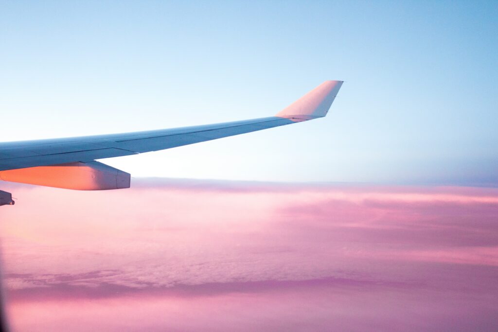 フライト中の飛行機から窓の外の翼を写した写真。ピンク色の雲が画面下に広がっている。