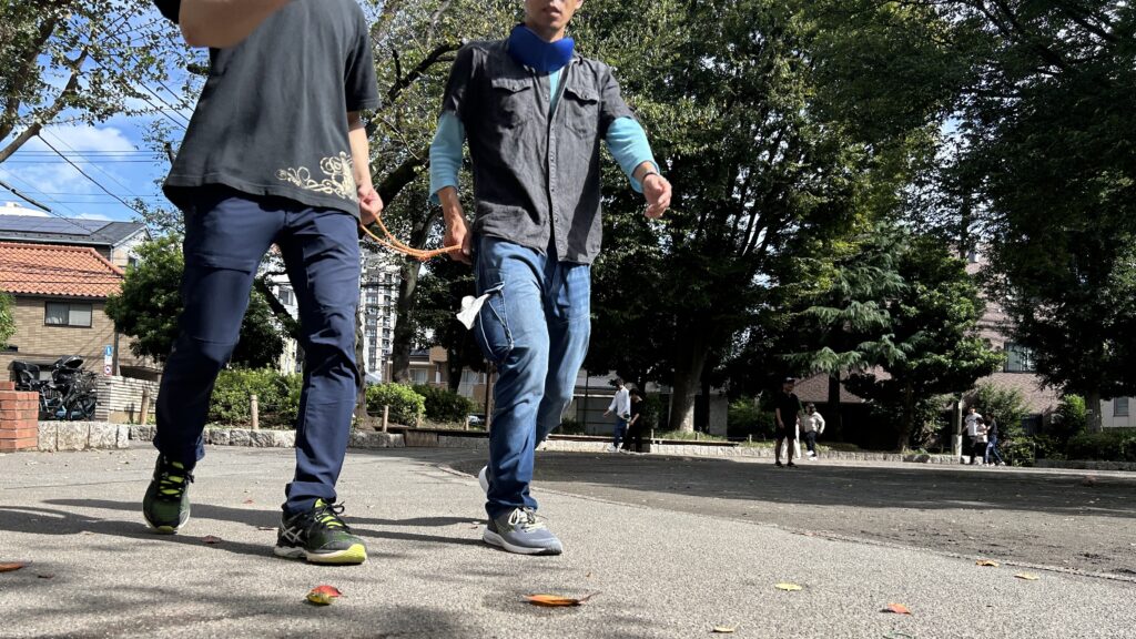 公園の中を、輪にした紐を持ちながら二人組で走っている様子。