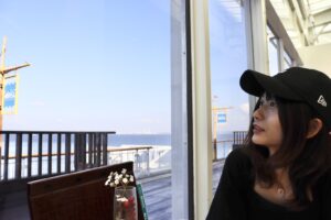 海辺のレストランのテラス横の席で、海を眺めている、黒いキャップをかぶったみーちゃん。