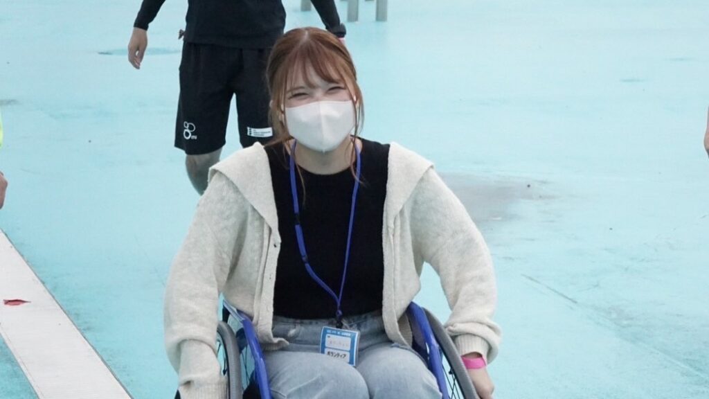 車いすの体験をしている、マスク姿のあだっちゃん。目元から満面の笑みが伝わる。