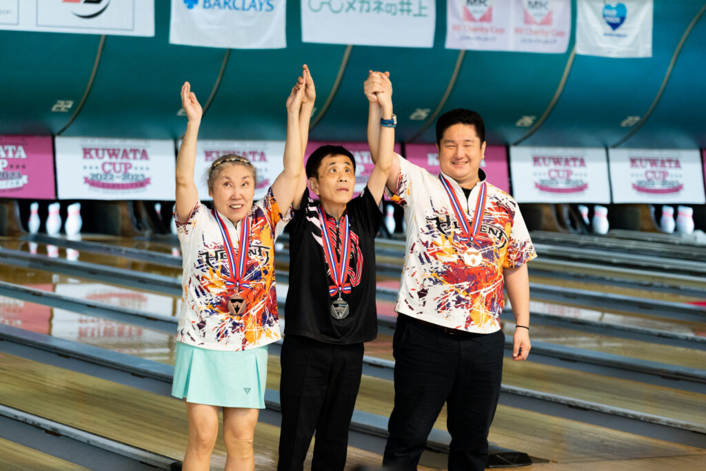 レーンを背に、つないだ手を掲げ、表彰台に立つ3人の写真。一番右が井上さん。