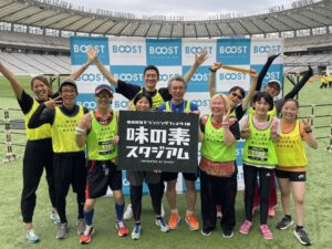 大会参加時の集合写真。「BOOSTランニングフェスタIN味の素スタジアム」と書かれたパネルをもって、笑顔でポーズをしているメンバーの皆さん。