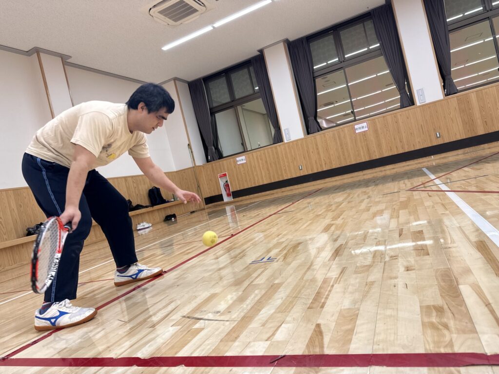 室内でブラインドテニスをプレー中のg筆者。前傾姿勢で空中のボールをラケットがとらえようとしている様子。
