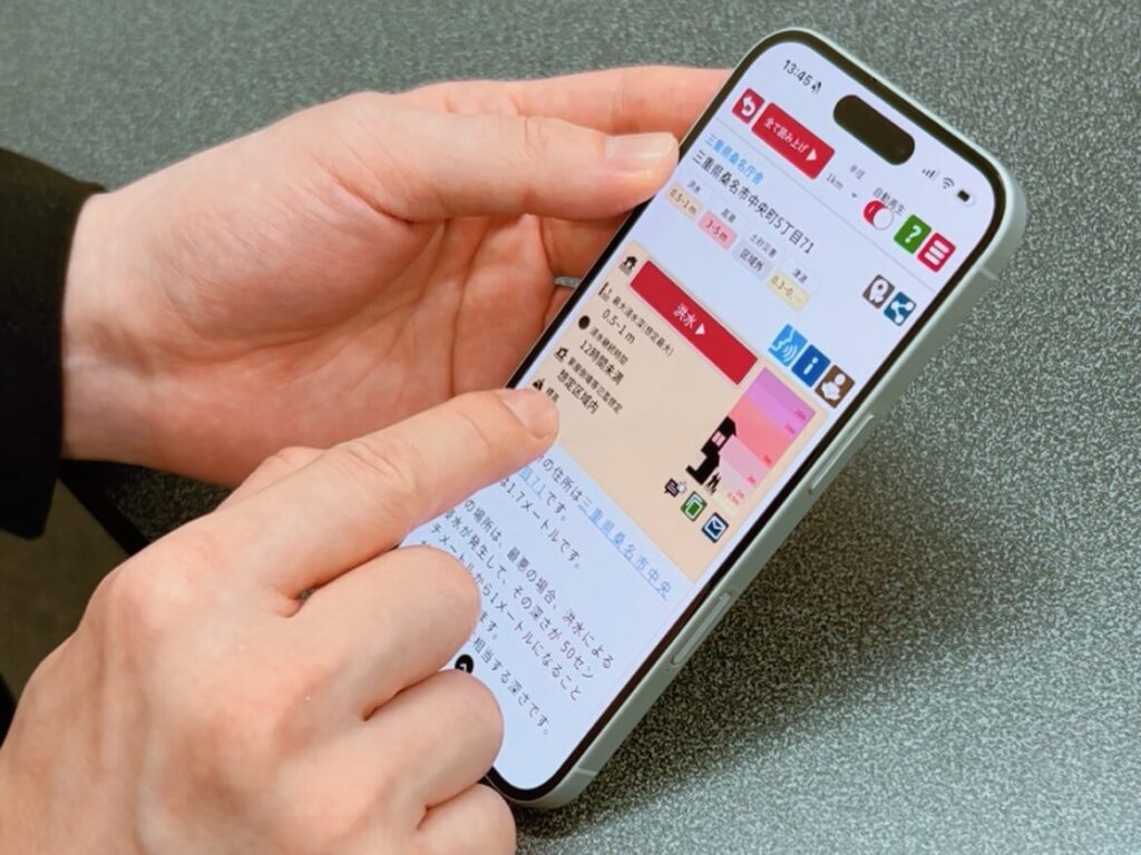 「耳で聴くハザードマップ」のスマートフォン画面を操作している手元のクローズアップ写真。