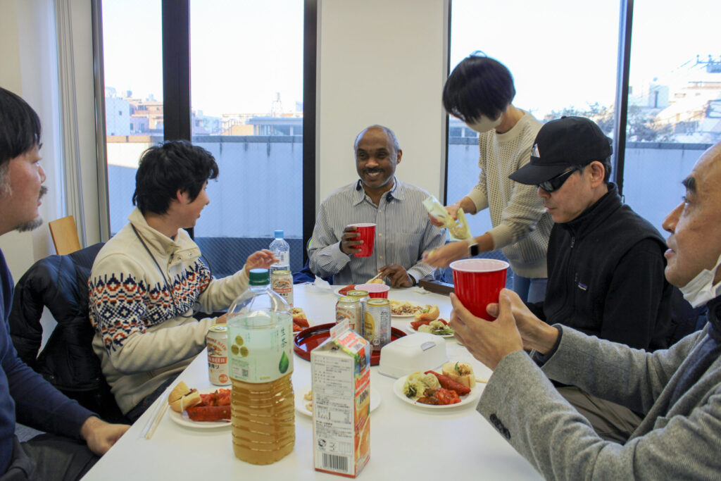 交流会の様子。参加者4人と大坪さん、サポートの方一人の合計6人。お菓子や軽食、飲み物などが机に置かれ、みなさん笑顔。