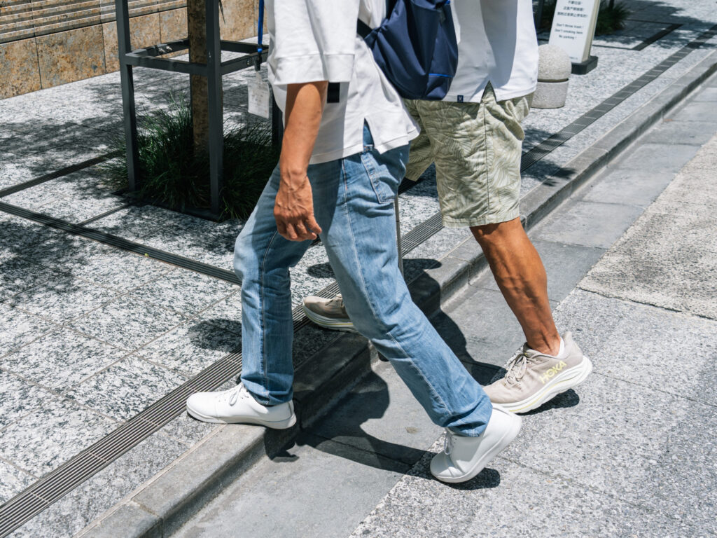 ガイドヘルパー役と視覚障害者役の2人の男性が、歩道を並んで歩く足元。段差を超えている瞬間の様子。