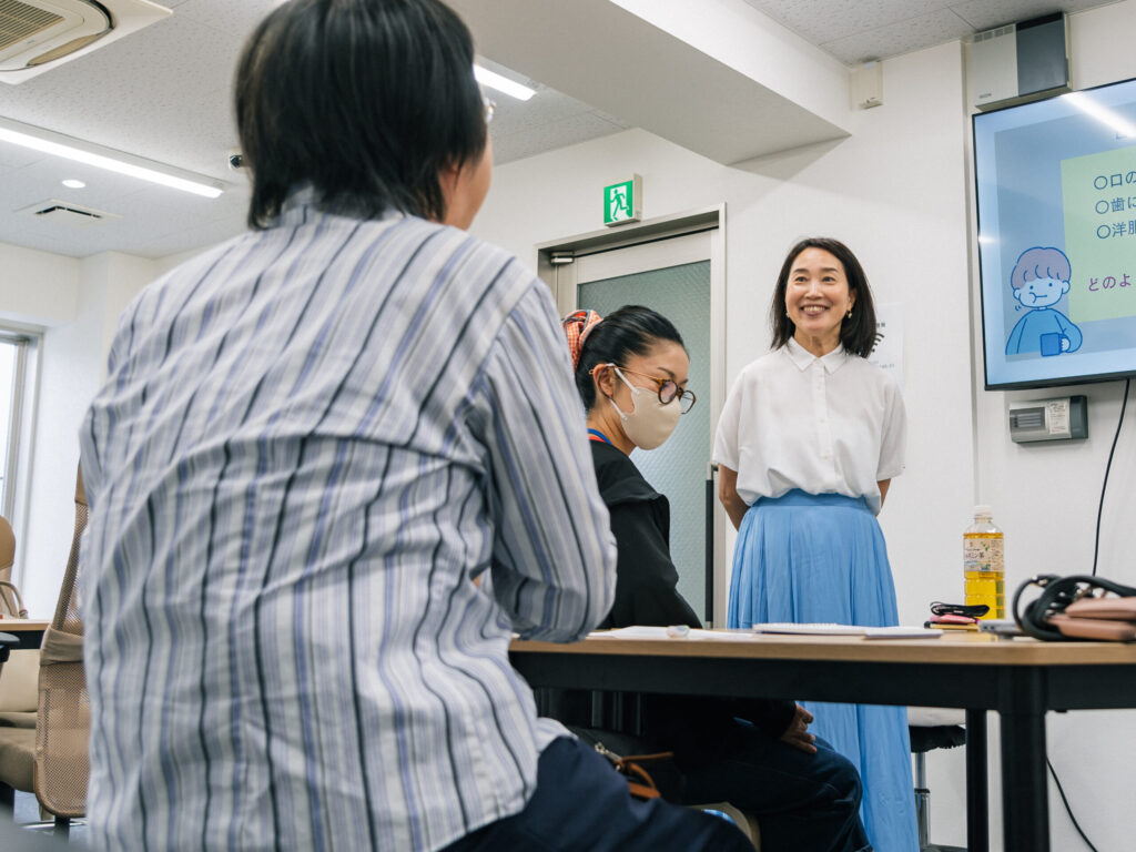 笑顔で参加者と対話をしている野村さん。姿勢が良く、前髪をあげているので表情が良くわかる。