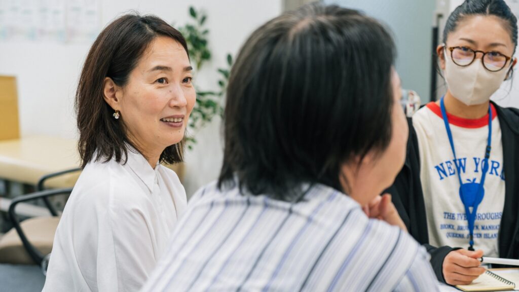 参加者と一緒に円卓につき、微笑みながら参加者の発言を聞く野村さん。