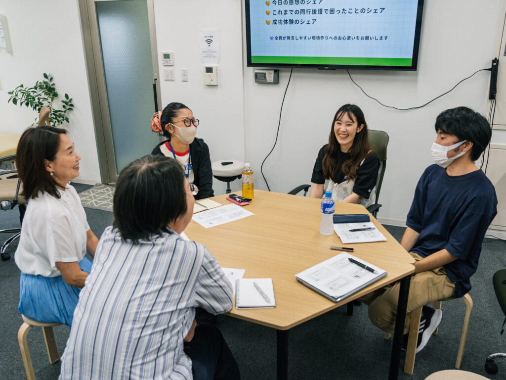 参加者の円卓に参加して、笑顔で話している運営メンバーの土屋さん。講師の野村さんと参加者も笑顔。