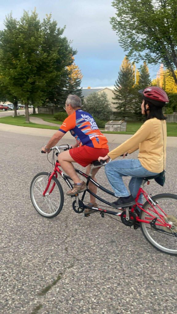 2人乗り専用のタンデム自転車の前に乗るホストファーザーと、後ろに乗るかなうさん。住宅街の中を走っている。