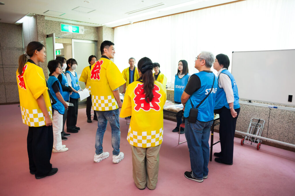 イベント前に入り口で集まって打合せをするスタッフ。中央には代表の高橋さんの姿がある。