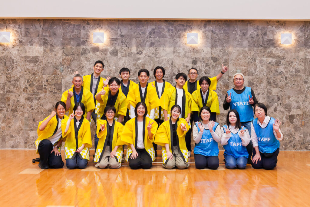 みつきスタッフとサポートメンバーの集合写真。視覚障害者のサポートメンバーもいる。黄色いハッピかSTAFFと書かれた青いビブスを着ている。