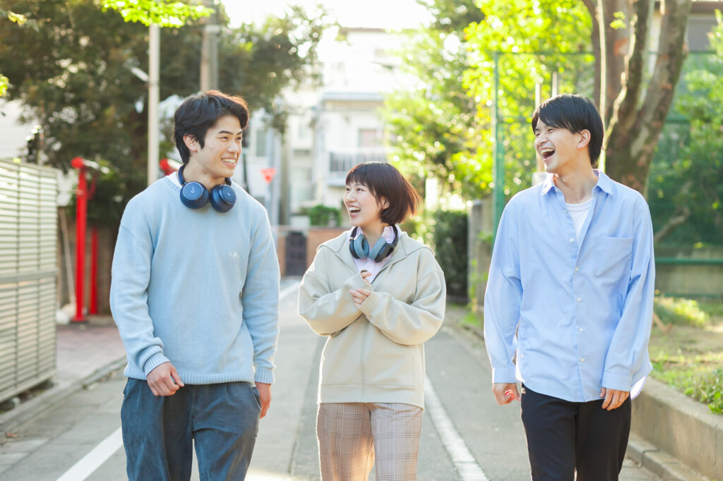 若い男女が3人、笑顔で公園の脇の道路を歩いている画像。