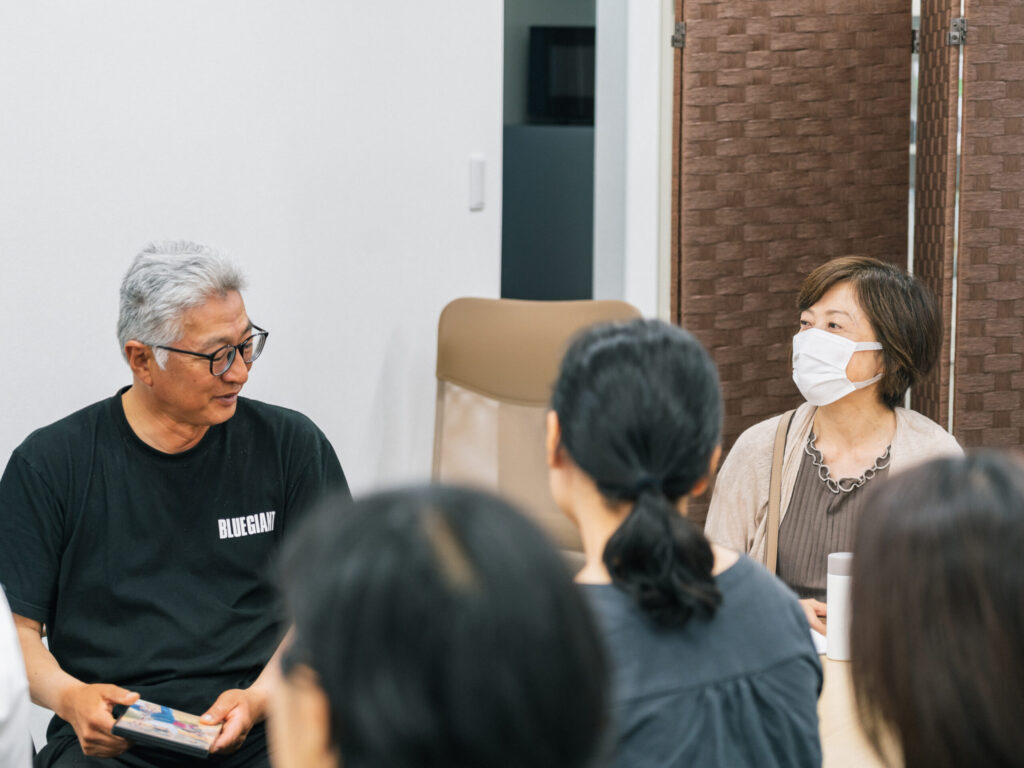 参加者が檀さんを囲んで話している様子。参加者の方を向きながら手を膝に置き話している檀さん。