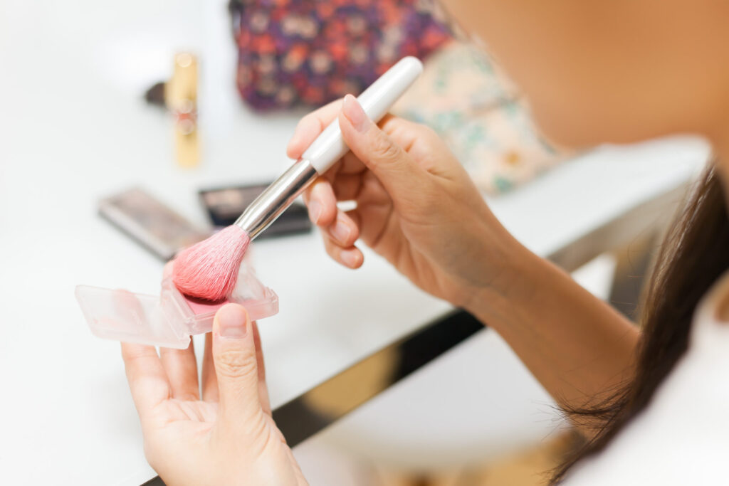 右手にメイクブラシを持ち、チークをブラシの毛先になじませている手元の写真。
