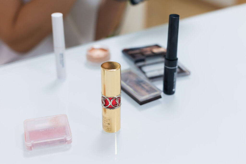 白いデスクの上に置かれた化粧品。口紅、アイシャドウ、アイライナー、チーク、コンシーラーなど。