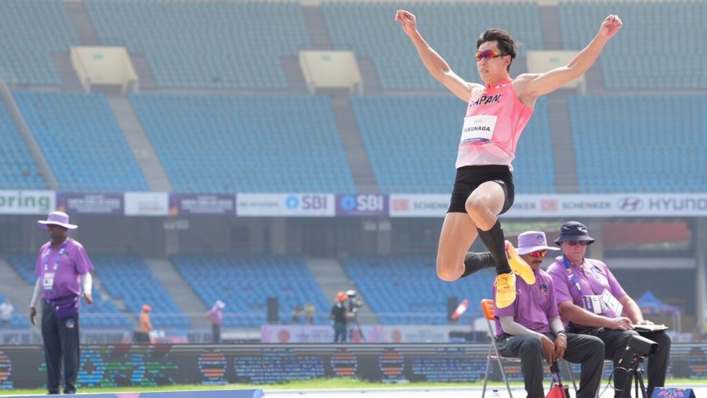 走り幅跳び競技中の福永選手。両腕を大きく上にあげ、胸をそらして両ひざを曲げ空中を飛んでいる瞬間。