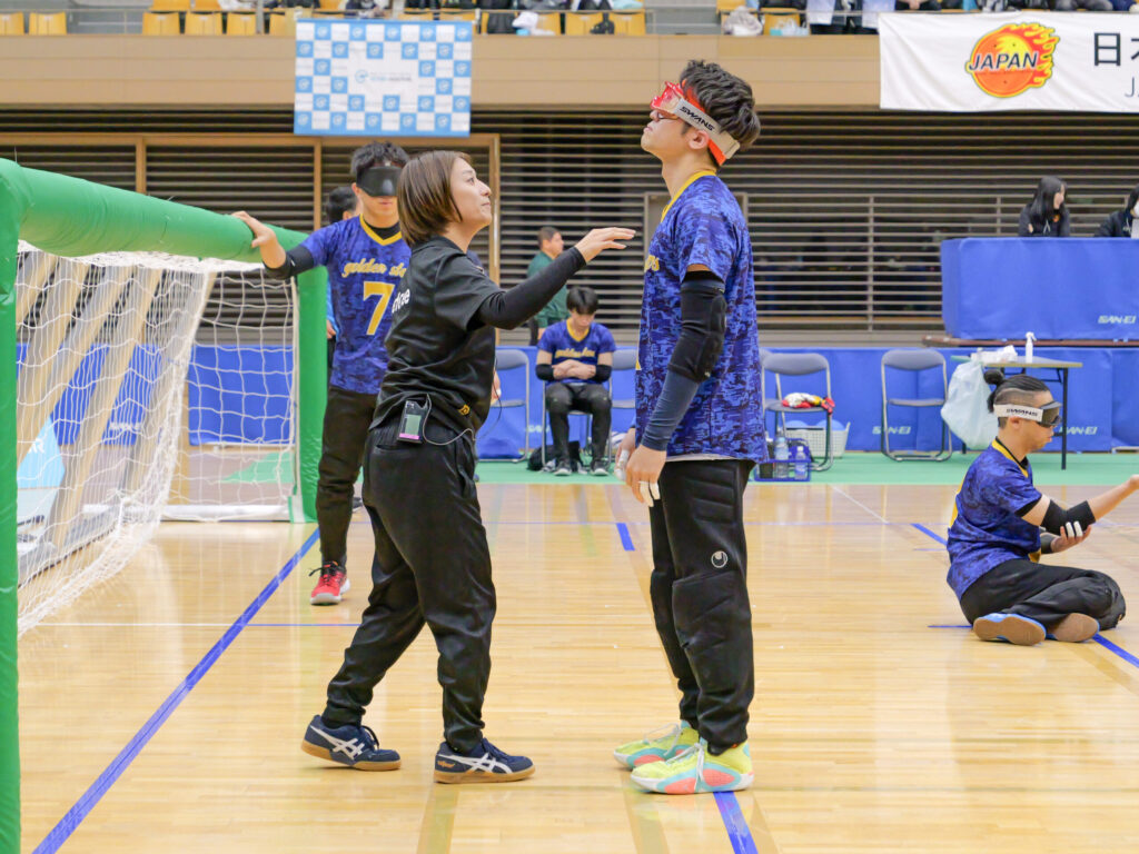 アイシェードを装着し、上を向いている選手と、その前で装着状況を確認するレフェリー。