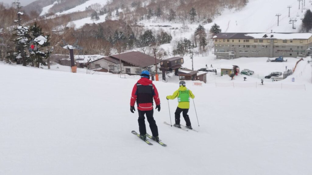 筆者ケビンさんが雪の斜面を滑っている。ケビンさんの後ろからガイドが声をかけている。