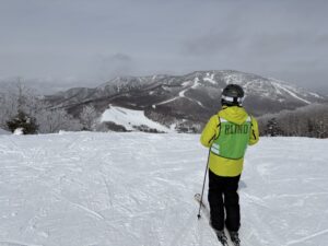 筆者ケビンさんが、スキー場のスタート位置に立っている。明るい黄色のウエアで、「BLIND」と書かれた黄緑色のビブスをウエアの上から着用している。