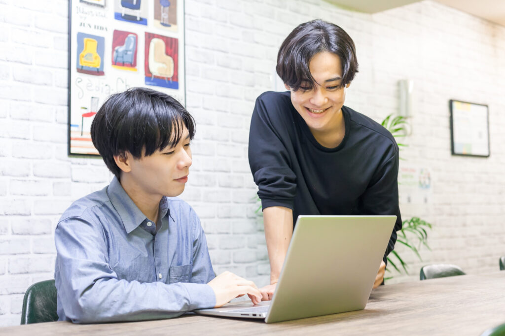 男性二人がノートパソコンを見ながら笑顔で話している様子。