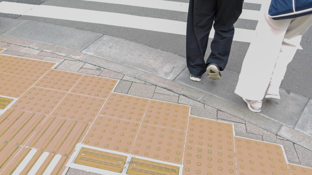 横断歩道の手前の歩道にある点字ブロックの写真。横断歩道に足を踏み出した木村さんと石井さんの足元が見える。