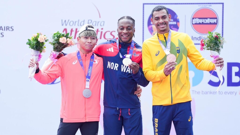 ニューデリー世界パラでのメダル授与後の上位3人のメダリストの写真。一番左が久野選手。首にメダルをかけ花束を持っている。