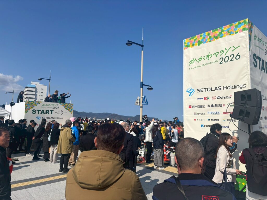 かがわマラソン2026のスタート地点の様子。人がたくさんいて、大会名が書かれた看板や「START」の標識などがある。