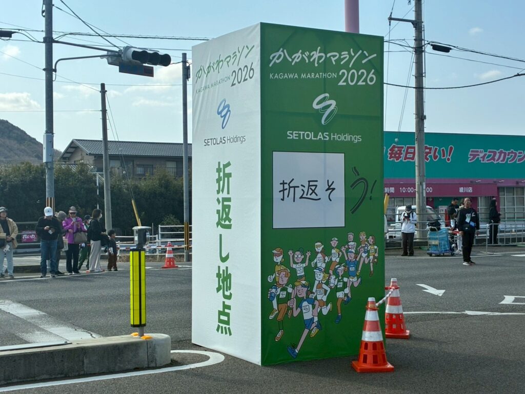 「かがわマラソン2026」と書かれた大きな折り返し地点んの目印。緑色と白を基調とした2メートル以上高さがある四角柱の形。