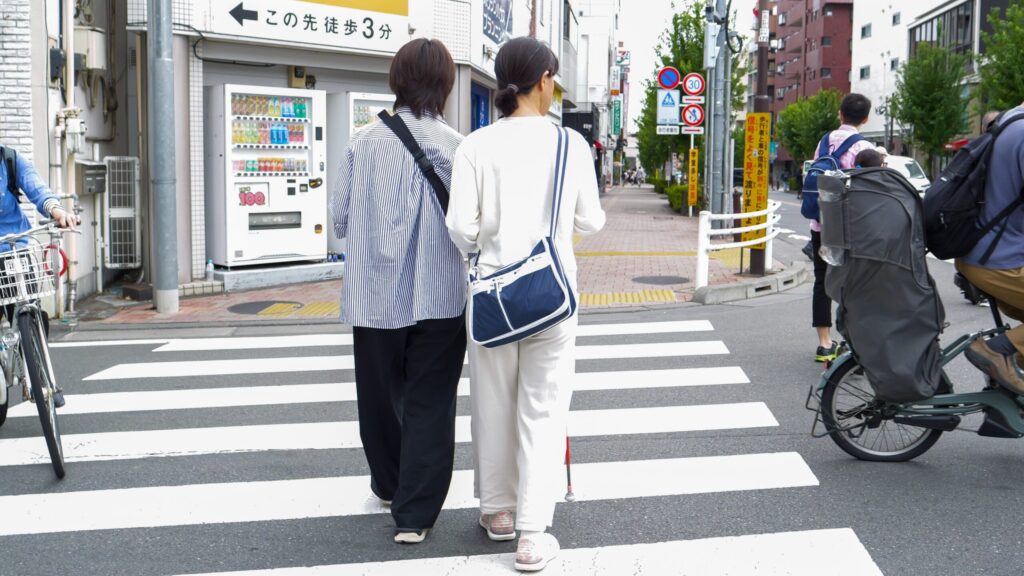 街の中の横断歩道をわたっているヘルパーの木村さんと石井さん。周囲には自転車も多く通っている。