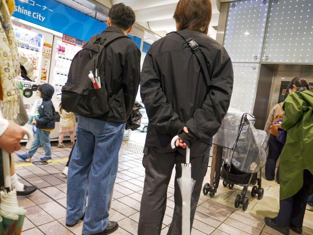 人混みの多い駅構内に立つ木村さんと秋山さんの後姿。