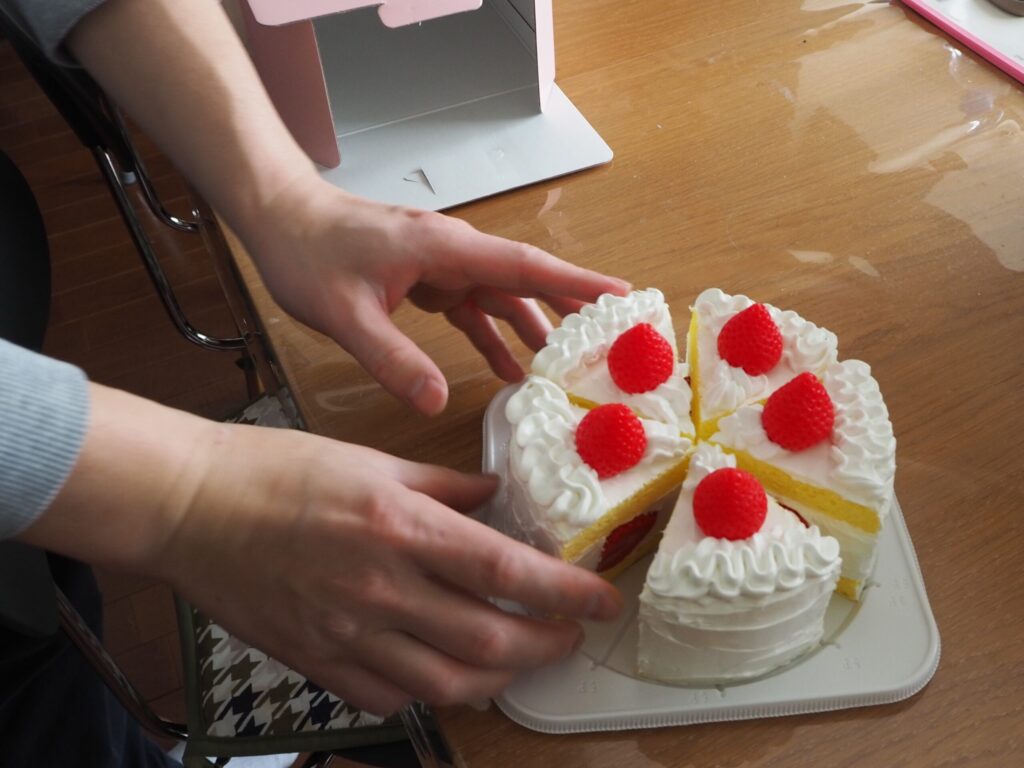 テーブルの上に置かれたデコレーションケーキの食品サンプル。齋藤さんが手で触れている。