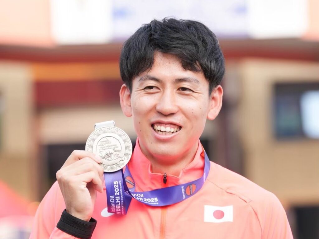 銀メダルを手に持ち、笑顔の福永選手。日本国旗のついた赤い代表ジャージを着ている。