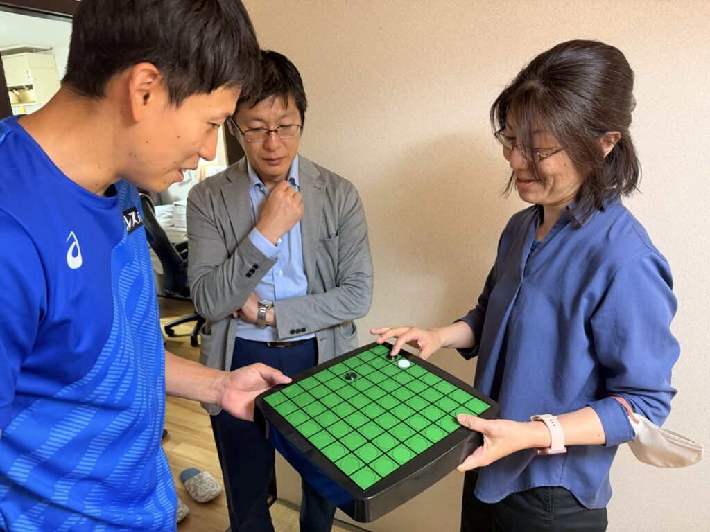放課後ルームいちごのスタッフが、指で回転して遊べる一体オセロを福永選手に見せているところ。