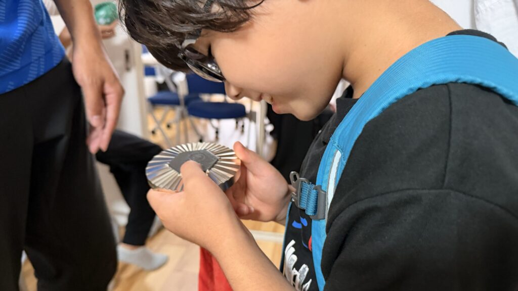 銀メダルを両手にそっと持ち、顔を近づけて観察している小学生。