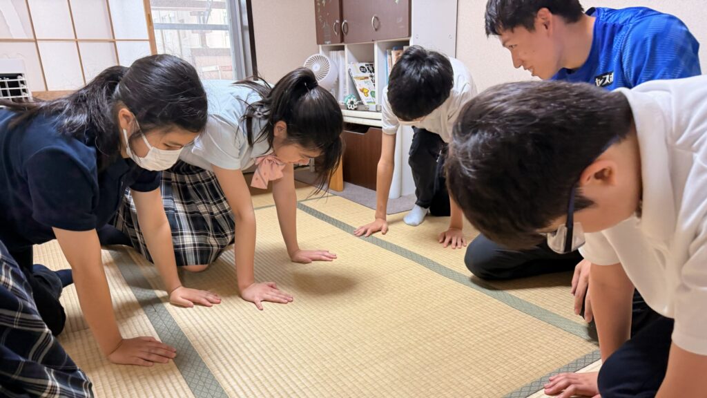 室内の畳の上で、制服姿の中学生4人に腕立て伏せの姿勢を教える福永選手。