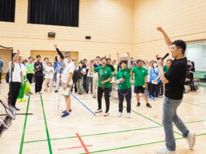 ブランインドスポーツエキスポ2026で、左手でマイクを持ち、参加者の前に立つ高橋さん。高橋さんと参加者が右手のこぶしをあげて「おー！」と声を出している。
