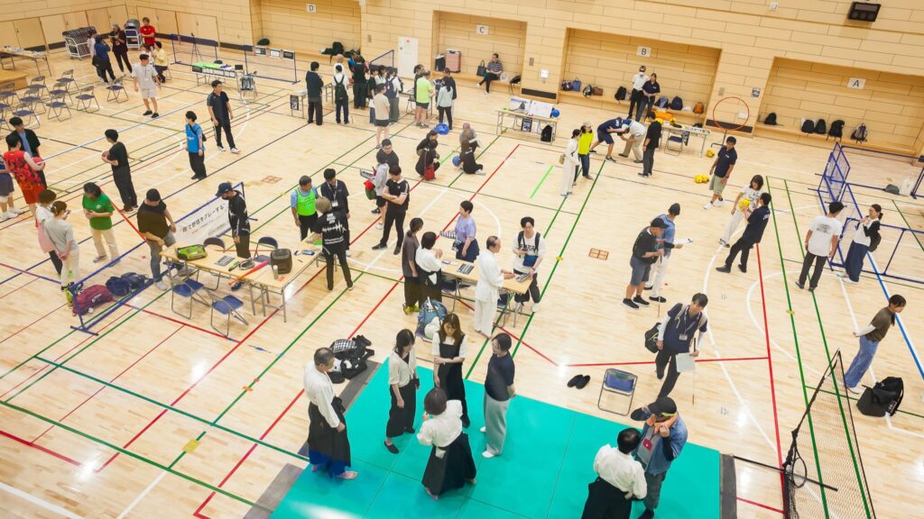 ブラインドスポーツエキスポ2026会場全体を上からとらえた写真。広い体育館内でそれぞれのスポーツのブースで体験している人たちがいる。