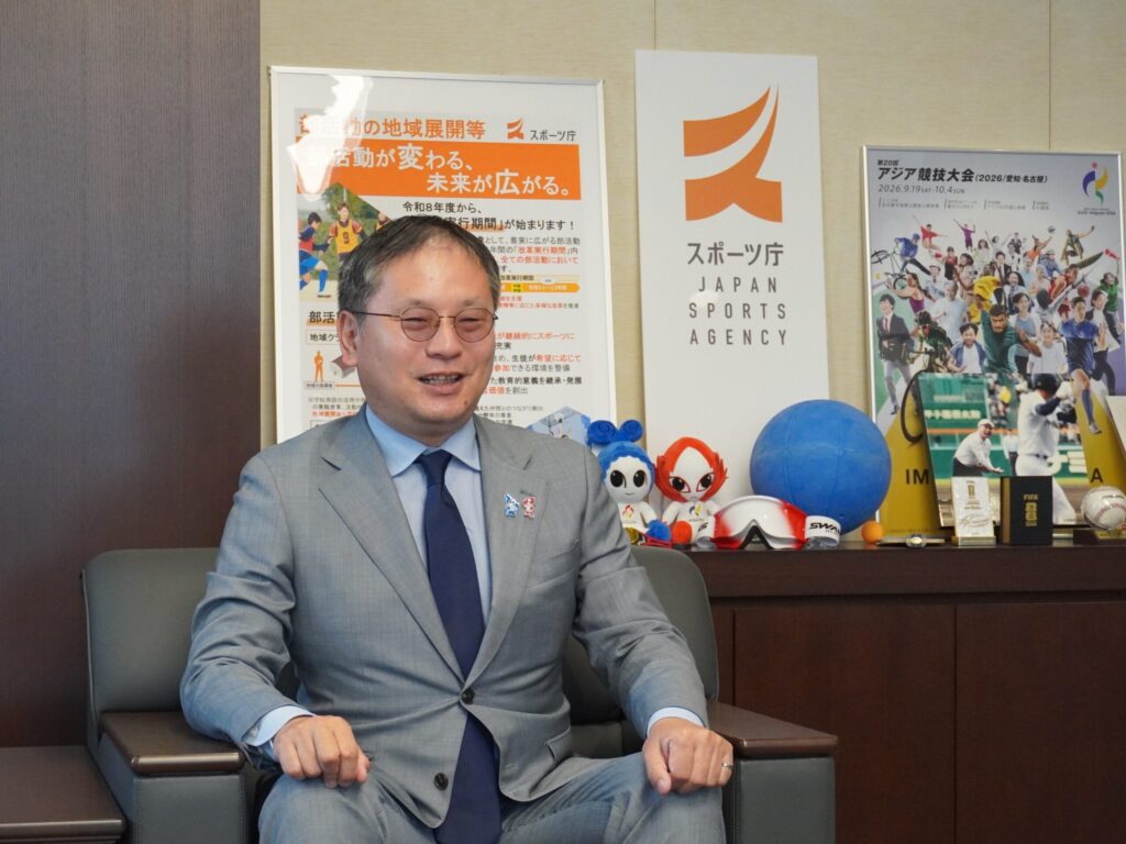 笑顔でインタビューに答える、グレーのスーツ姿の河合さん。スポーツ庁内長官室にて。