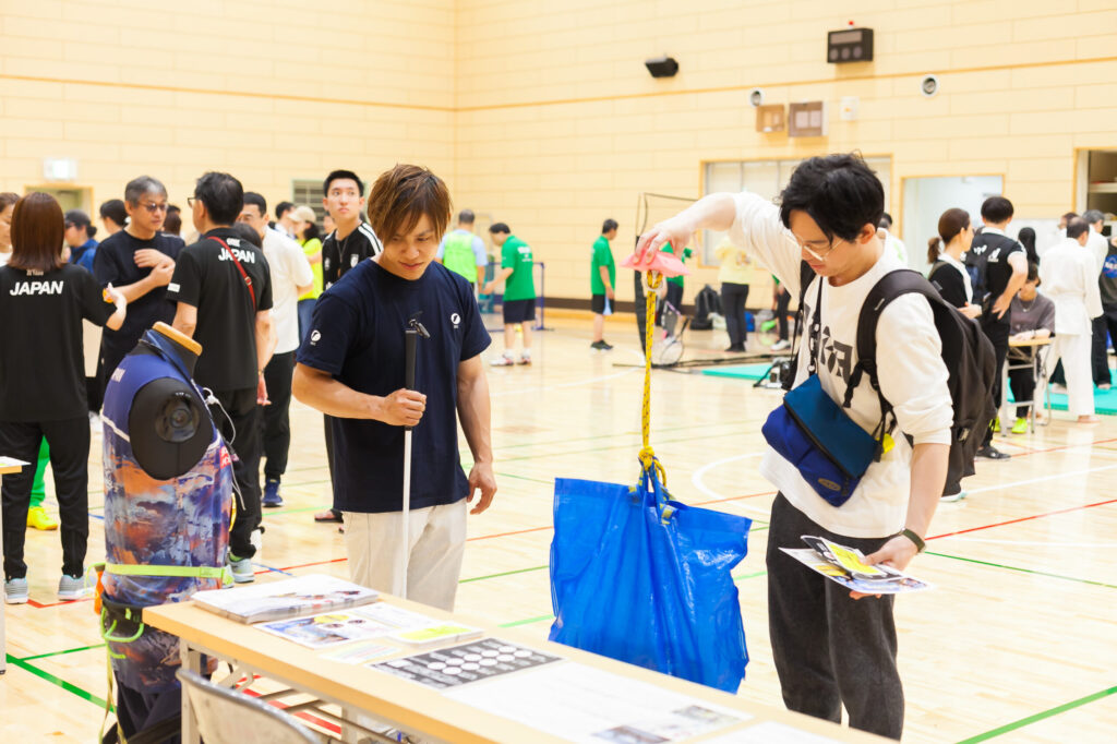 参加者に説明をしている濵ノ上選手と、重りを入れた袋を持ち上げて体感している参加者。